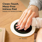 Close-up of an adult hand gently pressing a baby's hand onto a round Clean-Touch inkless pad. Text reads "Mess-Free Inkless Pad, Leaves no residue". Shows 3.4 inch (8.6cm) size. Demonstrates safety for sensitive skin and paws.