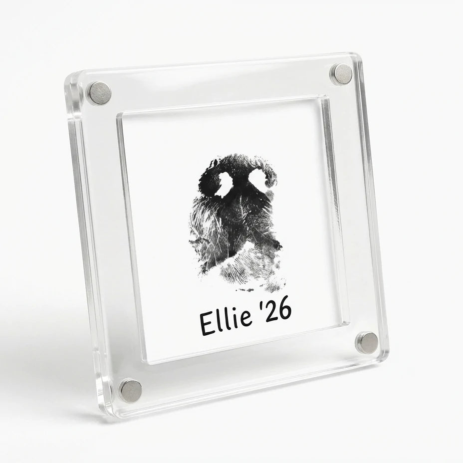 A clear acrylic magnetic frame holding a customized black dog nose print card reading "Ellie '26", attached to a stainless steel refrigerator door. Perfect as a pet memorial keepsake. Main image