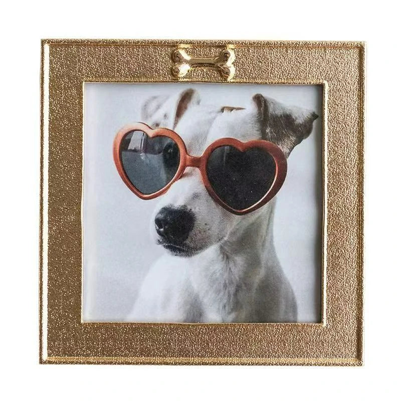 Hand touching the top detail of a gold pet memorial frame. Focuses on the raised dog bone emblem and the granular gold surface. A thoughtful and durable sympathy gift for dog lovers to display a personalized nose print of their best friend.