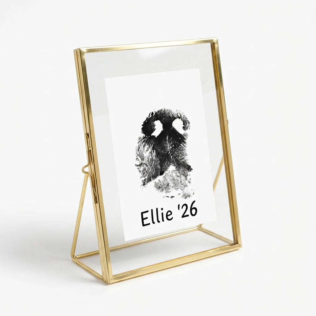 A touching pet memorial keepsake featuring a custom dog nose print stamped in black ink on white paper, floating inside a luxury gold metal glass frame. The personalized artwork includes the pet's name and year. Designed as a bereavement gift for loss of a dog, this standing photo frame elegantly showcases the unique details of a pet's nose, offering a lasting tribute and comfort for pet parents dealing with the loss of their best friend Main image