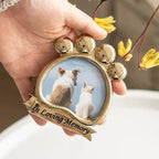 Close-up of a gold metal pet frame held in hand. The unique paw-shaped design features an engraved 'In Loving Memory' banner. Frames a cute dog and cat image. A durable and elegant memorial piece to honor a furry friend's life.