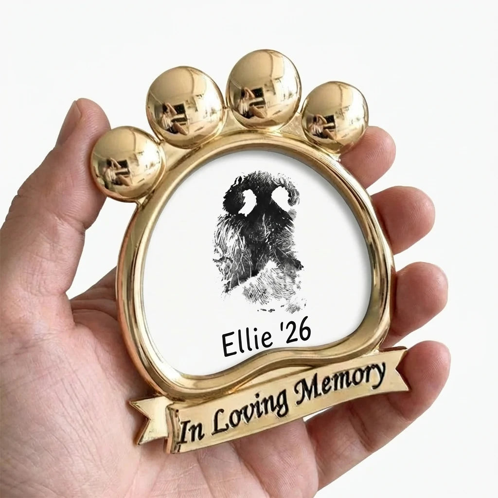 A touching pet sympathy gift being gently held in hand. This shiny gold paw-shaped frame has an 'In Loving Memory' inscription on the base. It contains a personalized dog nose print art. A cherished handheld memorial for grieving pet owners to keep close.