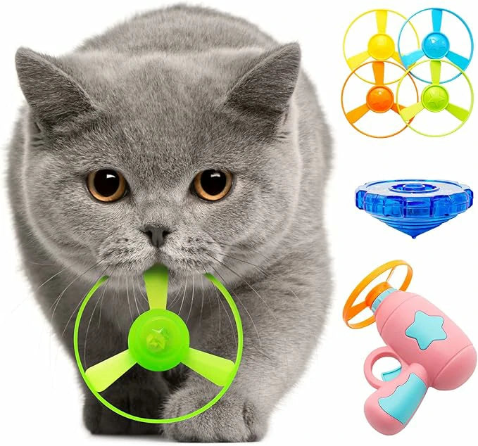 Grey British Shorthair cat holding a green flying saucer disc in its mouth. The image displays the Larleaf pink flying saucer gun launcher, colorful replacement discs, and a glowing gyroscope.