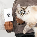 A person holding a fluffy cat and displaying a card with a clear black paw print created using the Larleaf clean-touch ink pad. This image demonstrates the detailed and mess-free result achievable with the kit.