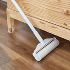 Larleaf sticky roller cleaning dust from wooden floor under furniture. Close-up view showing the adhesive surface effectively picking up debris in hard-to-reach areas.
