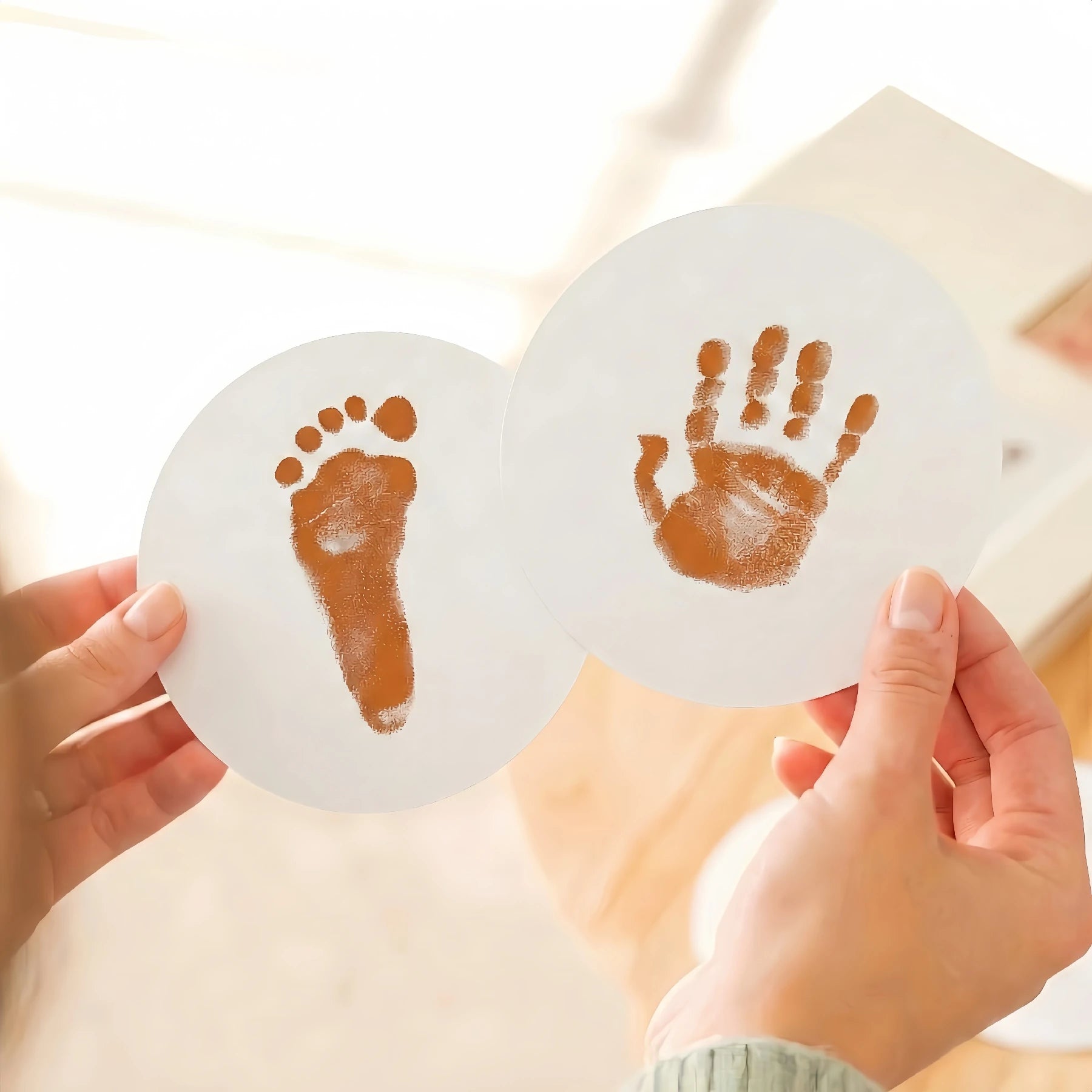 Close-up of a person's hands holding two round paw print keepsake cards featuring a high-contrast orange baby footprint and handprint. Demonstrates the detailed results of a orange ink print kit for DIY pet memorial goods.