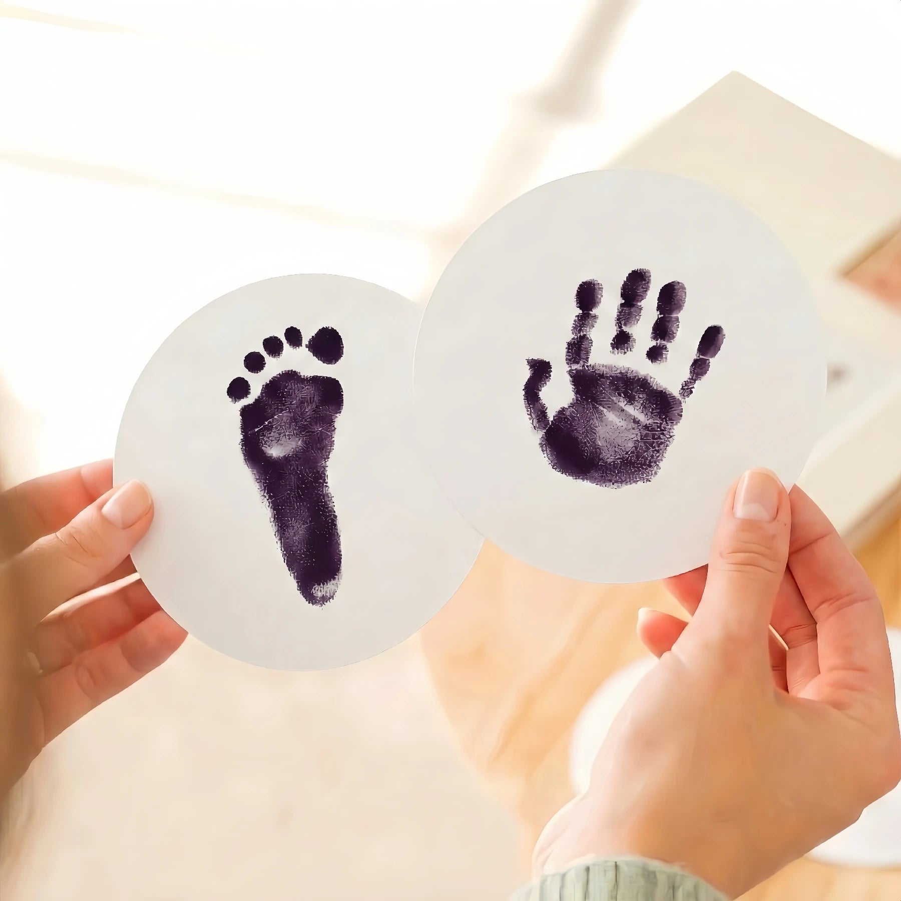 Close-up of a person's hands holding two round paw print keepsake cards featuring a high-contrast purple baby footprint and handprint. Demonstrates the detailed results of a purple ink print kit for DIY pet memorial goods.
