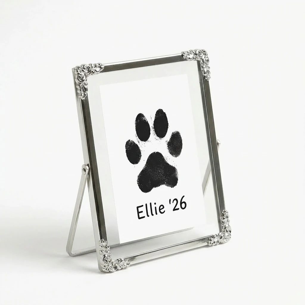 Freestanding silver memorial frame for a pet's paw print. Pictured from a 3/4 angle to show the elegant wire backing. The vintage floral details frame the artwork beautifully. A sophisticated sympathy gift for a desk or mantelpiece.