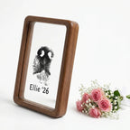 Hand presenting premium walnut wood floating frame with rounded edges. Shows distinct dog nose print (snout print) 'Ellie '26' suspended in double glass. Styled with roses to depict a touching, modern sympathy gift for pet loss remembrance