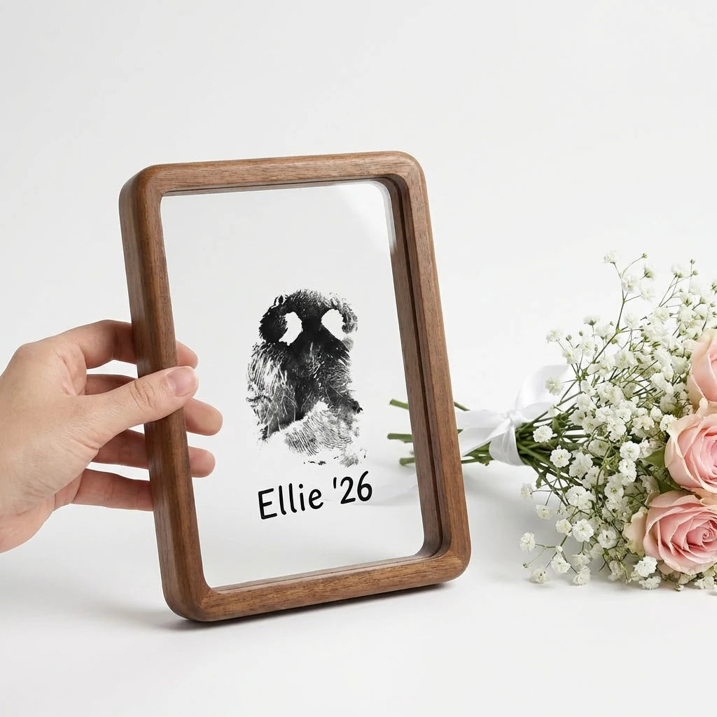 Hand presenting premium walnut wood floating frame with rounded edges. Shows distinct dog nose print (snout print) 'Ellie '26' suspended in double glass. Styled with roses to depict a touching, modern sympathy gift for pet loss remembrance